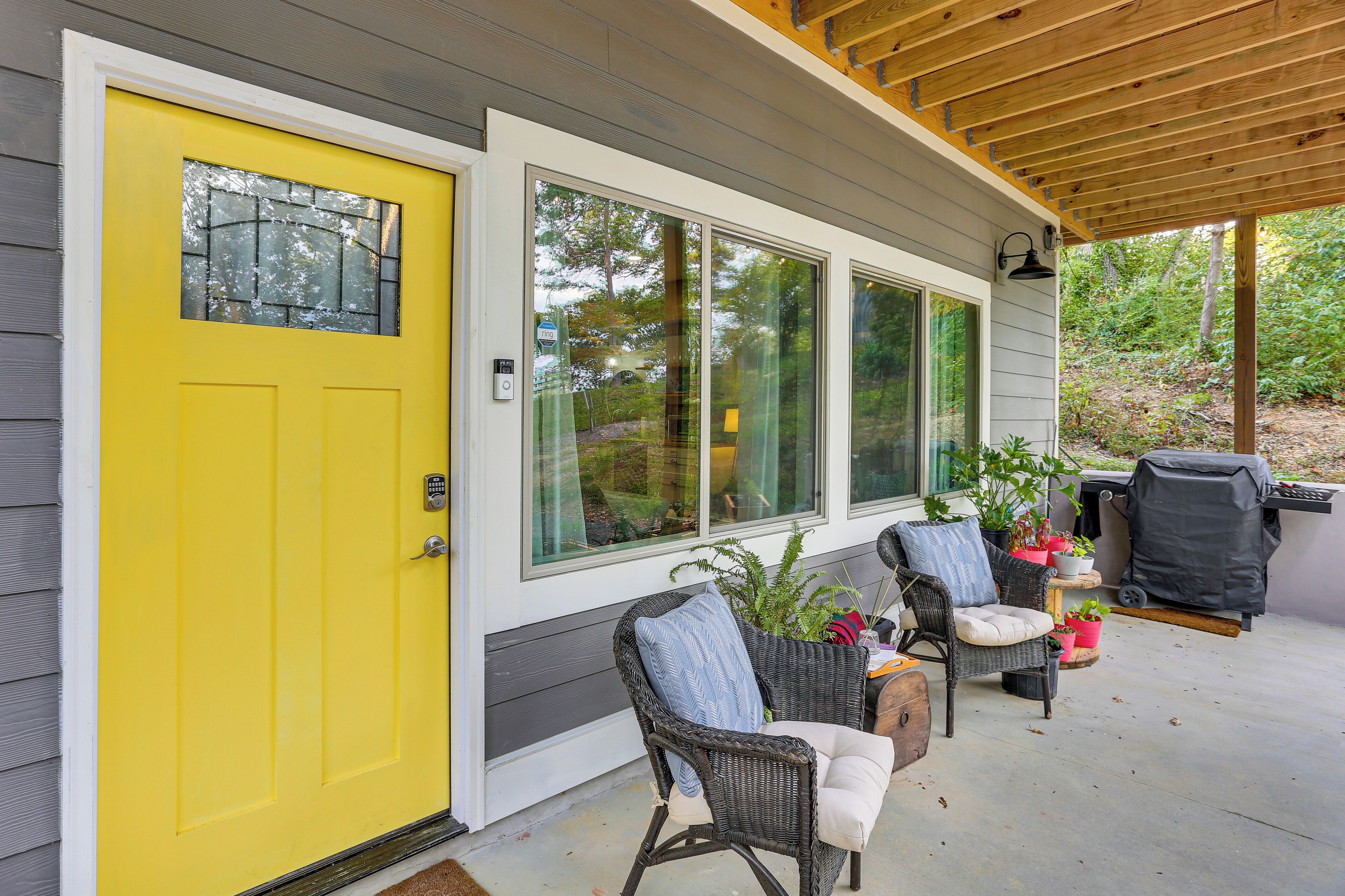 A covered porch with wicker furniture, a grill, and potted plants.