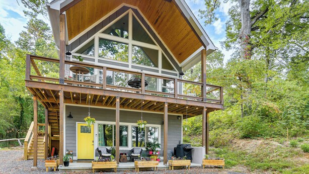 Eine zweistöckige Holzhütte mit einem Balkon, Sitzgelegenheit im Freien und einer Treppe, die zum oberen Stockwerk führt.