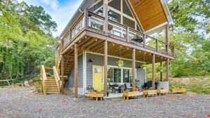 Eine zweistöckige Holzhütte mit einem Balkon, Sitzgelegenheiten im Freien und einer Schotterauffahrt.
