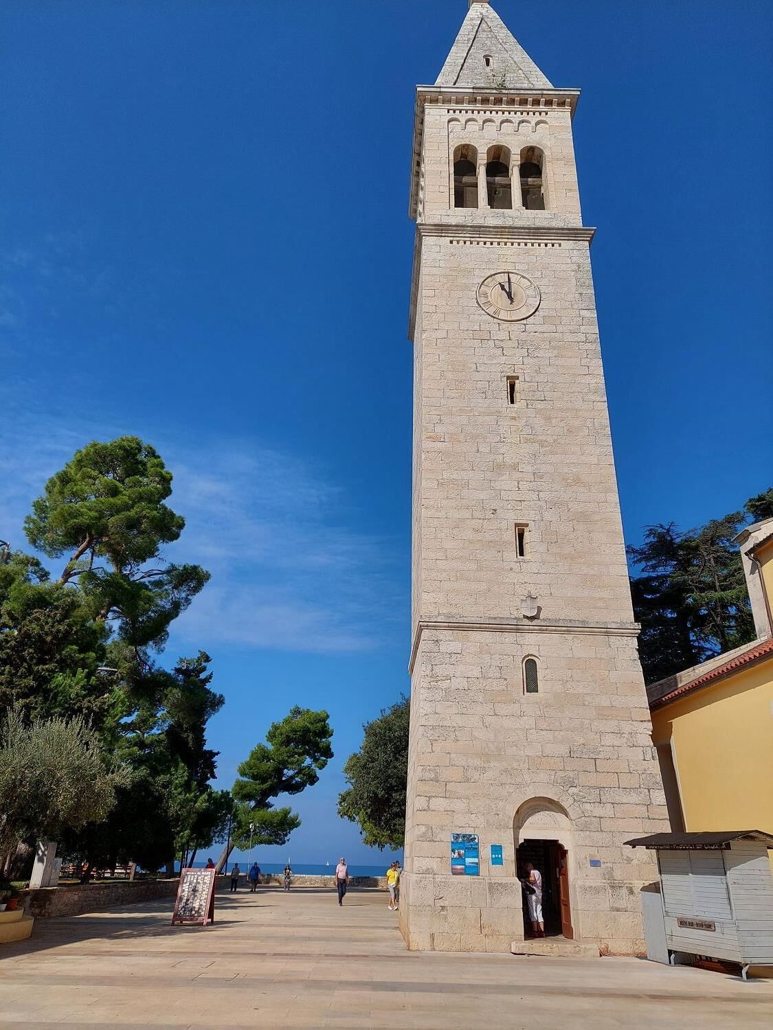 Una alta torre de piedra con un reloj, una puerta y un letrero pequeño.
