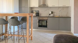 A modern kitchen with grey cabinets, a stainless steel range hood, a coffee maker, and a built-in oven. There is a wooden dining table with four chairs. - Renovated apartment with private terrace, WiFi, parking near Novigrad (Novigrad)