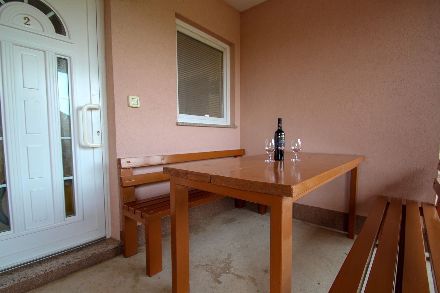 A room with a wooden table, a bench, a bottle of wine, and two glasses.