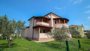 Ein zweistöckiges Gebäude mit Balkon, umgeben von viel Grün und blauem Himmel.
