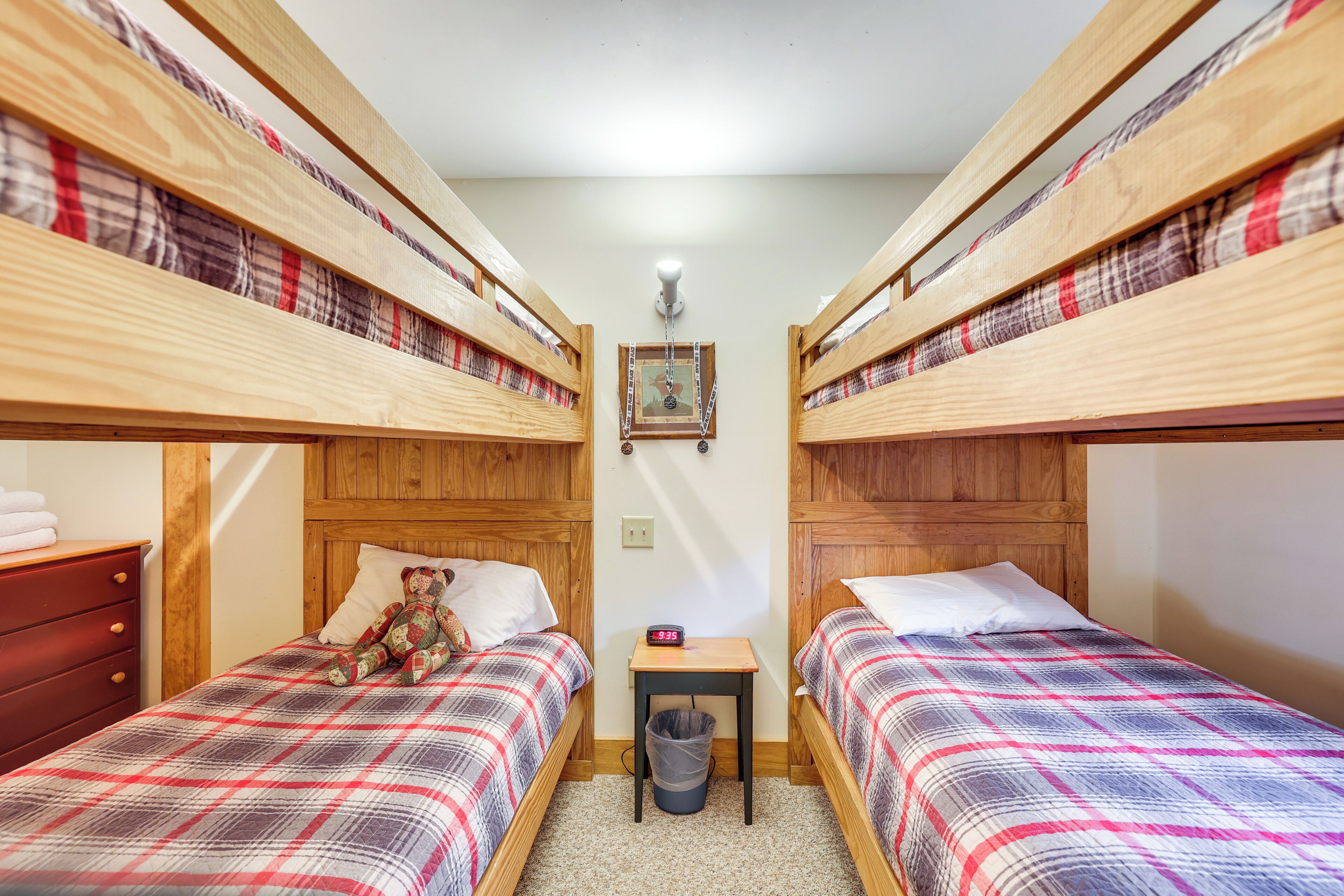 Una habitació amb dos llits superposats de fusta, una taula petita amb un rellotge i un os de peluix sobre un dels llits.