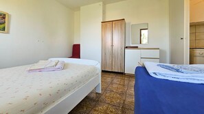 A hotel room with two beds, a wooden wardrobe, a small desk, and a mirror.