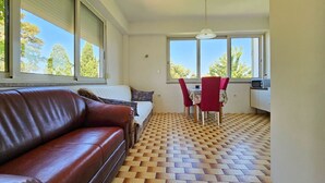 A room with a brown leather sofa, a bed with white bedding, a red chair, a small table with a radio, and a patterned floor. - Affordable, dog-friendly apartment just 100 meters from the beach (Dalja)