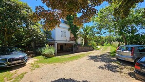 A gravel driveway leading to a white building with a covered porch, parked cars, and lush greenery. - Affordable, dog-friendly apartment just 100 meters from the beach (Dalja)