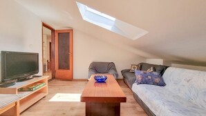 Ein gemütliches Wohnzimmer mit Fernseher, Couch, Holz-Couchtisch und einem Oberlicht.