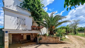 Ein zweistöckiges Gebäude mit einer Stein-Fassade, einem Balkon mit Sitzgelegenheiten im Freien und einer Palme im Garten.