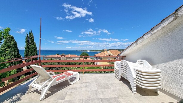 Ein Balkon mit Blick auf das Meer, einem roten Geländer und einer Reihe weißer Plastikstühle.