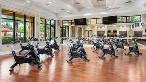 A gym with stationary bikes arranged in rows, large windows, and a flat wooden floor. - Bonita National Coach home, offers endless amenities for everyone  (Bonita Springs)