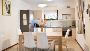 Una cocina moderna con armarios blancos, una mesa de comedor con cuatro sillas y un florero con flores secas sobre la mesa.