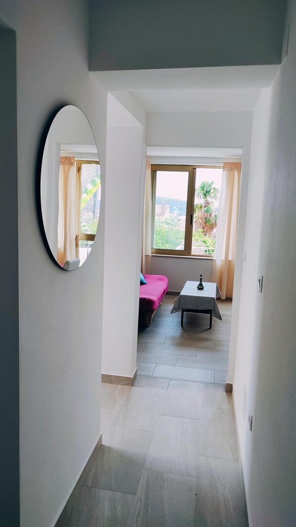 A narrow hallway with a large mirror on the left, a bed with a pink bedspread, and a small table with a vase in the center. - Charming apartment just 700 meters to the beach with terrace and balcony (Rovinj)