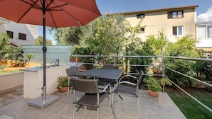Eine Terrasse mit Tisch, Stühlen, einem roten Sonnenschirm und Kübelpflanzen.