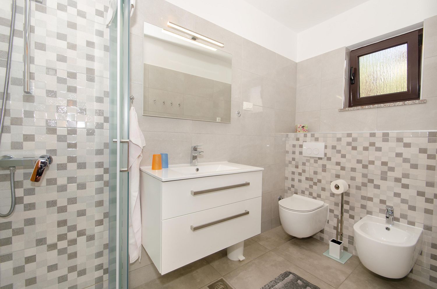 A modern bathroom with a glass shower enclosure, a white vanity with a mirror, a bidet, and a toilet.