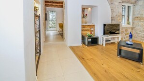 A modern living room with a stone wall, wooden flooring, a TV, and a small side table with a vase. - Stunning old town apartment with private terrace, outdoor shower - only 500 meters to the beach (Rovinj)
