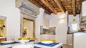 A dining area with a table set for four, a kitchen in the background, and a rustic ceiling. - Stunning old town apartment with private terrace, outdoor shower - only 500 meters to the beach (Rovinj)