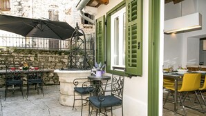 An outdoor café with stone flooring, metal chairs, and tables, featuring a stone fountain and green shutters. - Stunning old town apartment with private terrace, outdoor shower - only 500 meters to the beach (Rovinj)