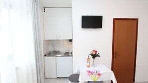 Una habitación pequeña y limpia con kitchenette, una mesa de comedor con sillas, un televisor montado en la pared y una puerta de madera.