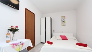 Un dormitorio con cama, escritorio y silla, armario y una mesita de noche con un jarrón de flores.
