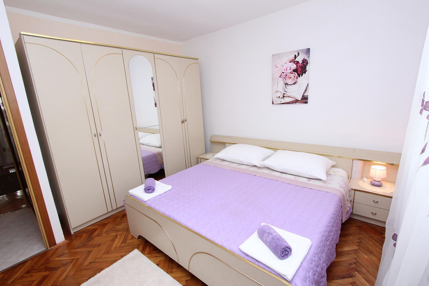 A bedroom with a bed, a nightstand, a lamp, a wardrobe, and a mirror.