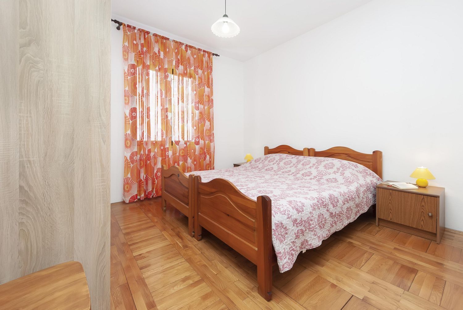 A bedroom with a wooden bed, a nightstand with a lamp, and a window with curtains.