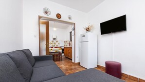 Un salon moderne avec un canapé gris, un petit pouf rouge et un téléviseur à écran plat fixé au mur.