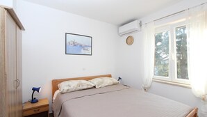 Un dormitorio con cama, mesita de noche, lámpara, reloj de pared, aire acondicionado y ventana con cortinas.