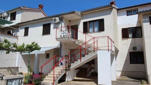 Un edificio de dos pisos con una escalera roja, paredes blancas y varios ventanales.