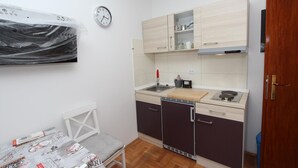 Cocina compacta con lavamanos, estufa y armarios, una mesa de comedor con una silla y un reloj en la pared.
