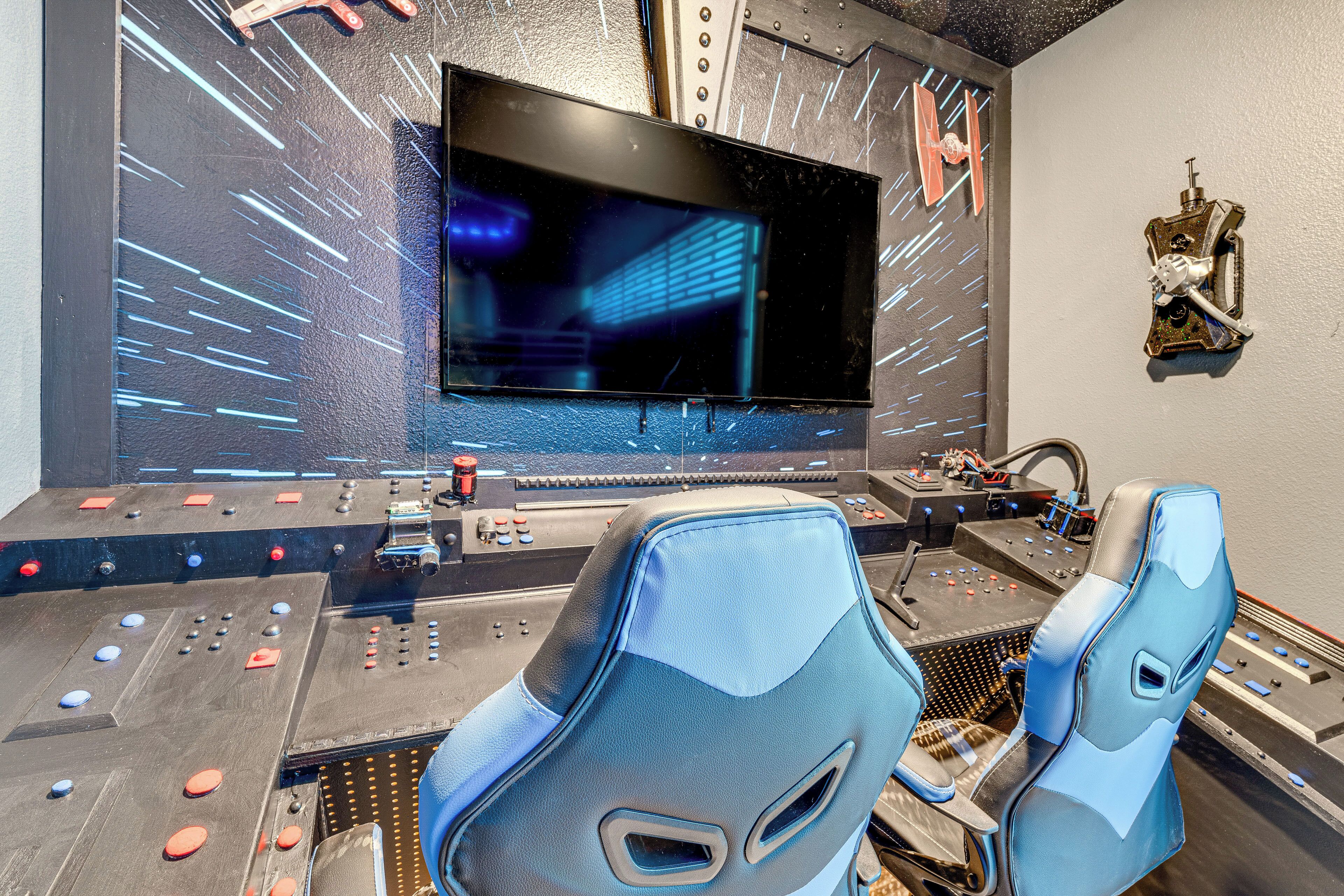 Une salle de contrôle dotée d’un grand écran, de fauteuils de jeu et de divers panneaux de commande.