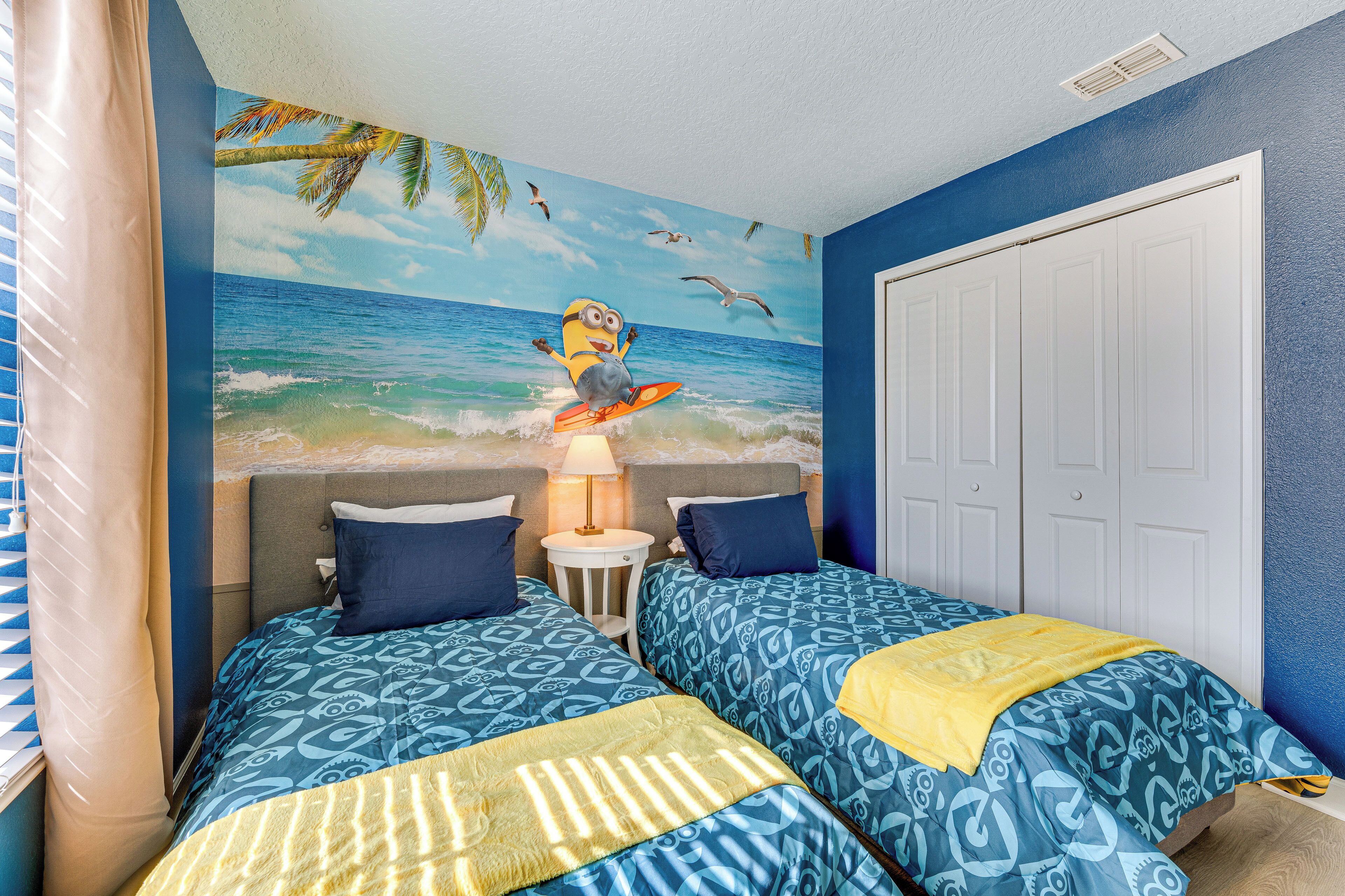 A room with two beds, a mural of a beach scene, and a white door.
