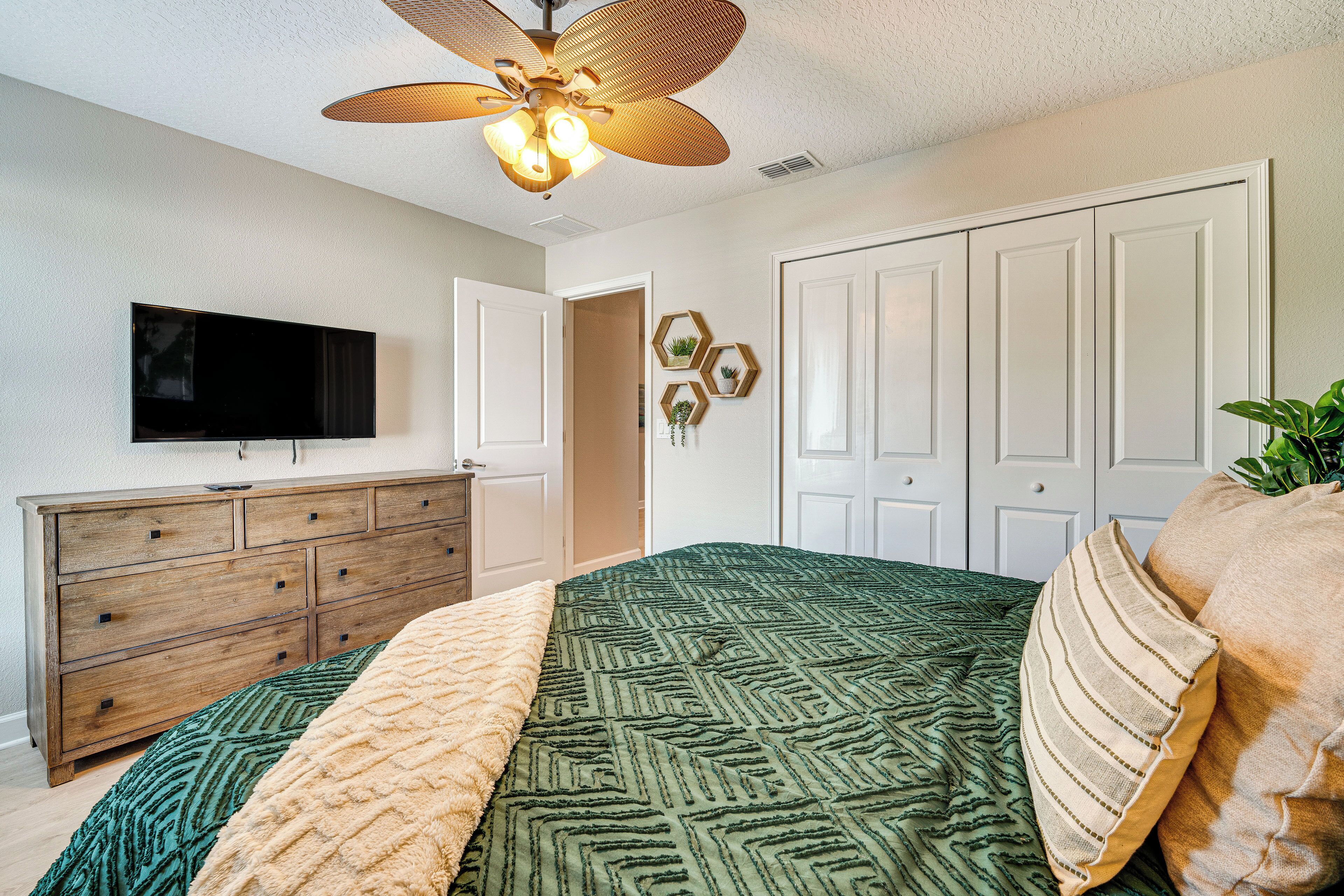 A bedroom with a bed, dresser, TV, and a ceiling fan.