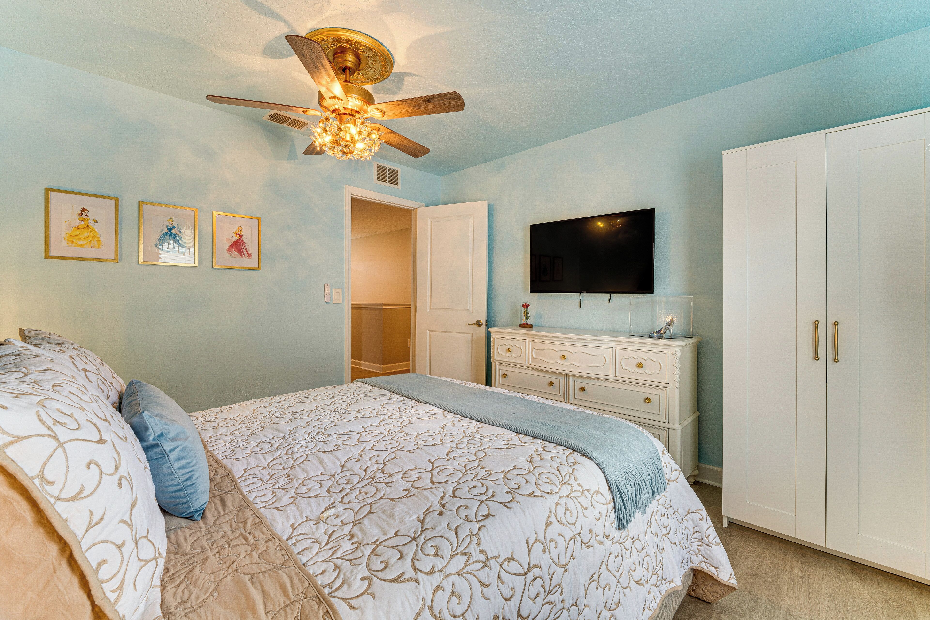 A bedroom with a bed, a dresser, a wardrobe, a ceiling fan, and wall-mounted artwork.