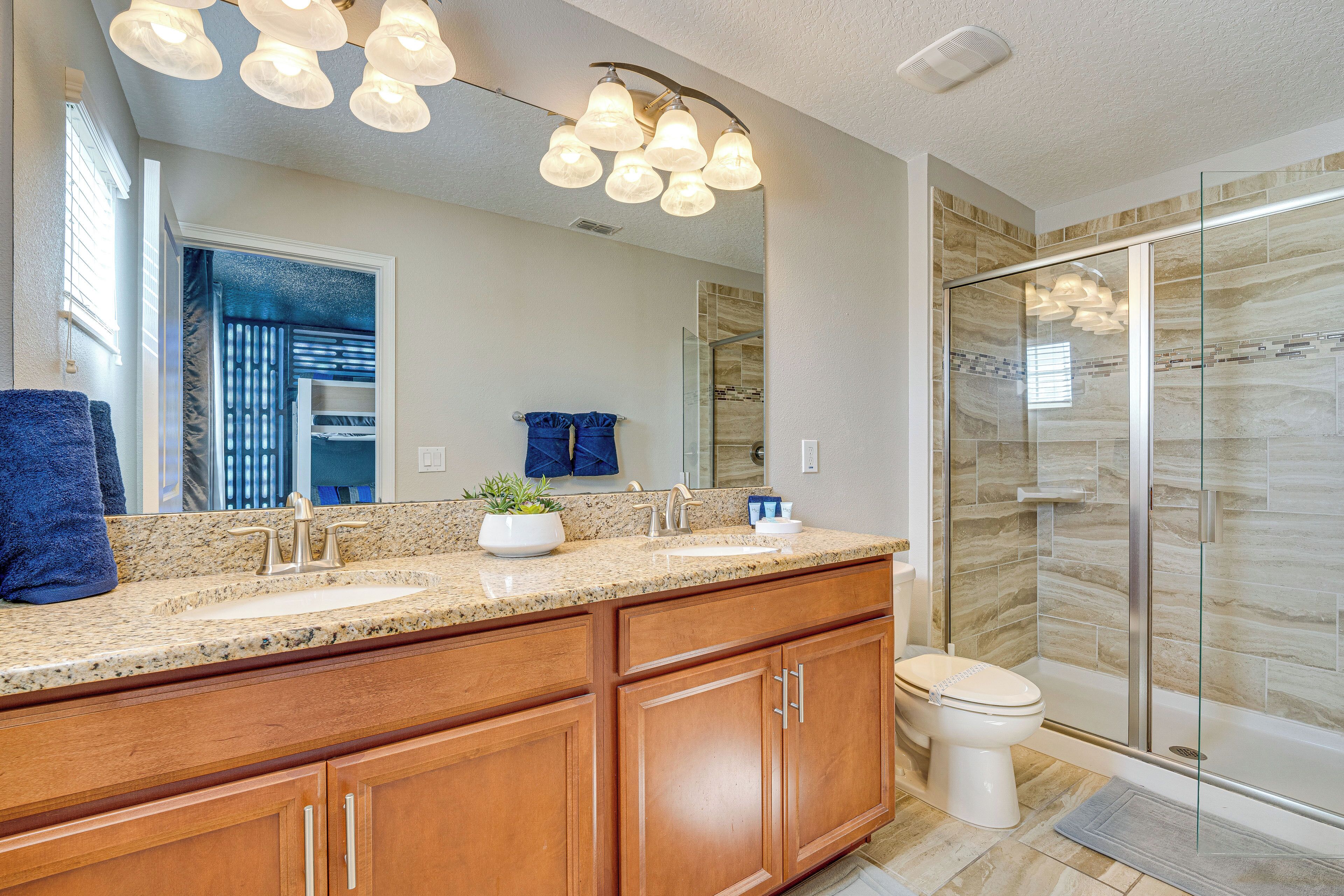 A modern bathroom with a granite countertop, wooden cabinets, a large mirror, a glass shower enclosure, and a toilet.