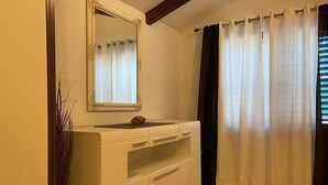A bathroom with a white vanity, a mirror, and a window with white curtains. - Mediterranean apartment with barbecue area, sun loungers in the garden, private parking, WiFi (Rovinj)