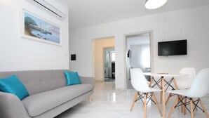 Un salon moderne avec un canapé gris, des fauteuils blancs et un téléviseur à écran plat.