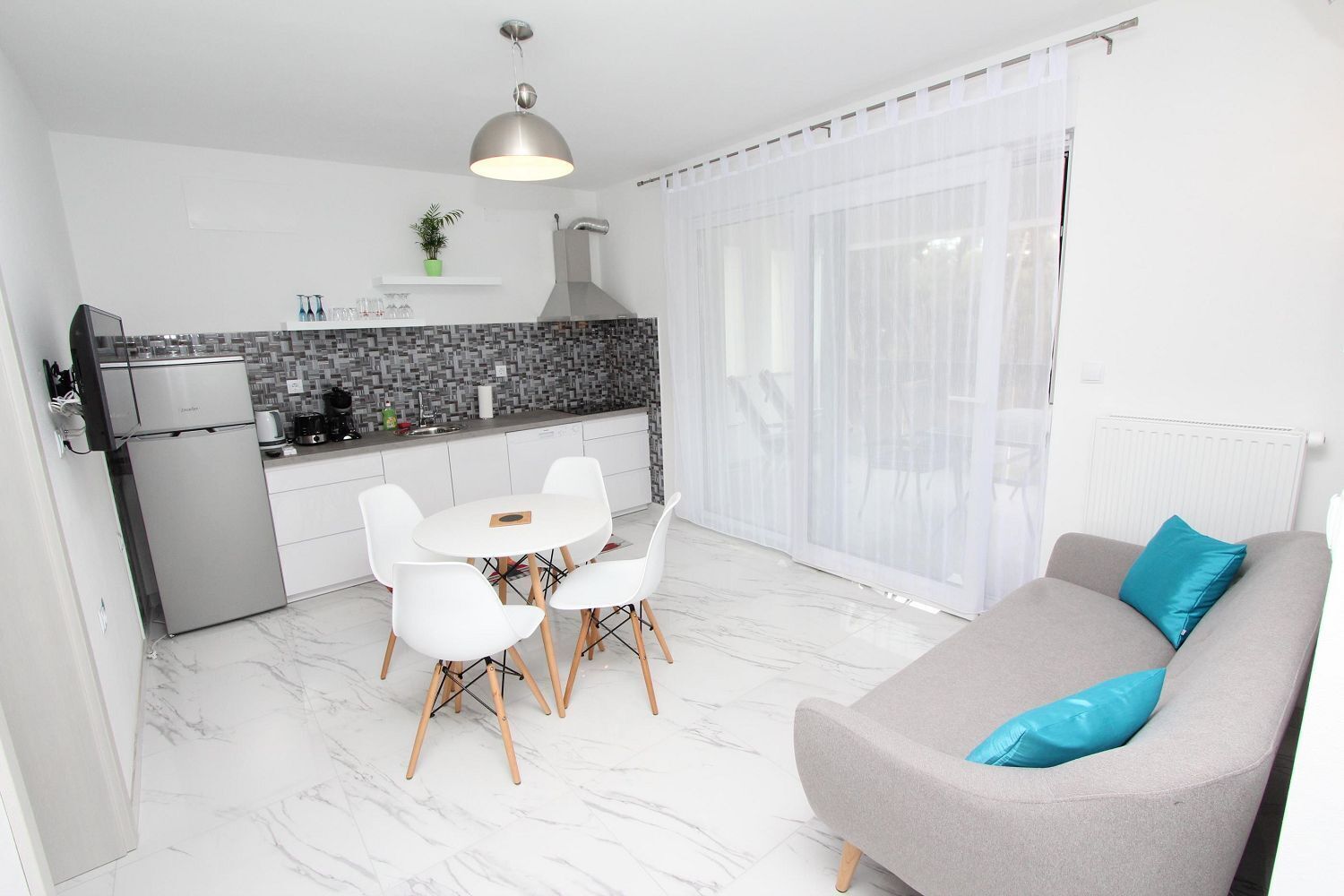 A modern kitchen with white cabinets, a built-in oven, and a dining area with a round table and white chairs.
