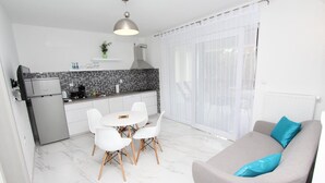 Une cuisine moderne avec des armoires blanches, un four encastré et un coin repas comprenant une table ronde et des chaises blanches.