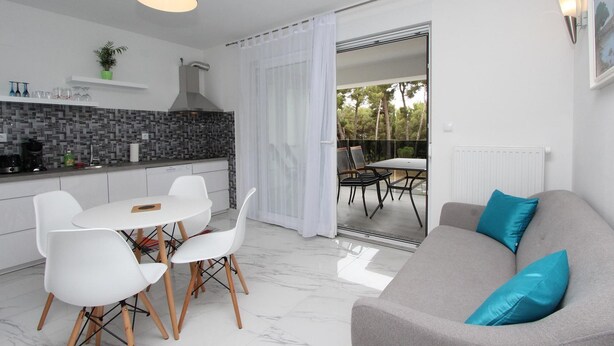 Une cuisine moderne avec des meubles blancs, un pare-feu noir en carreaux et un coin repas avec des chaises et une table blanches.