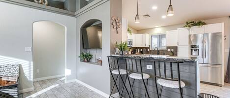 A modern kitchen with a bar area, stainless steel appliances, and a light wood floor.