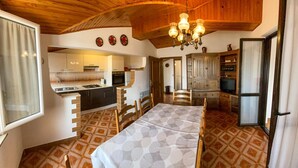 Una cocina compacta con electrodomésticos modernos, un comedor con mantel estampado y un techo de madera con candelabro.