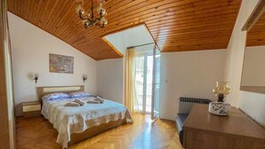Un dormitorio con techo de madera, una cama con colcha blanca, una mesita de noche, un radiador y una ventana con persianas.