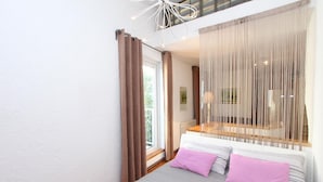 Ein Schlafzimmer mit einem Bett, einem Fenster, Vorhängen und Blick ins Freie.