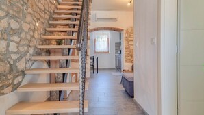 A staircase with wooden steps leading to a stone wall. A kitchen area with a stone countertop and a window is visible in the background.
