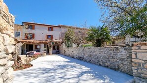 A stone-walled courtyard with a building featuring a tiled roof and wooden shutters.