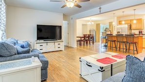 A modern living room with a flat-screen TV, a ceiling fan, and a dining area with wooden chairs and a kitchen in the background. - Near Skiing: Serene Harrison Retreat w/ Fire Pit (Harrison)