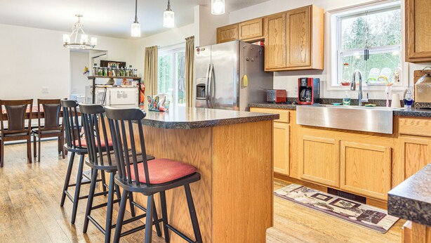 A modern kitchen with wooden cabinets, a stainless steel refrigerator, and a bar area with stools. - Near Skiing: Serene Harrison Retreat w/ Fire Pit (Harrison)