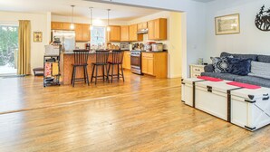 A modern kitchen with wooden cabinets, a central island with stools, and a dining area with a table and chairs. - Near Skiing: Serene Harrison Retreat w/ Fire Pit (Harrison)