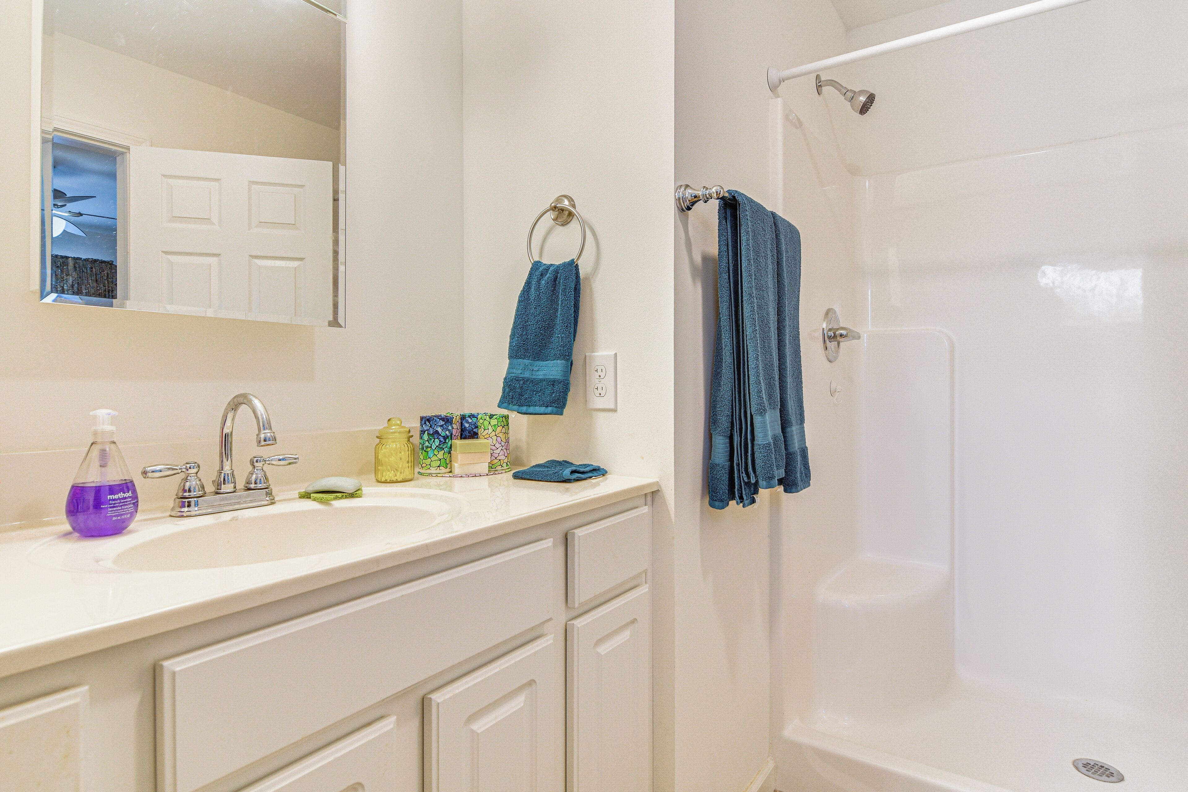 Une salle de bain avec un lavabo blanc, un miroir, un porte-serviettes avec une serviette bleue et un espace douche.